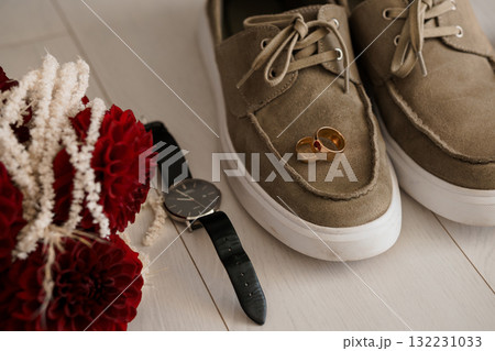 Wedding Details Flatlay: Rings, Watch, Brown Suede Shoes, Red Flowers, Groom's Accessories, Light Wood Background, Rustic Chic Style 132231033