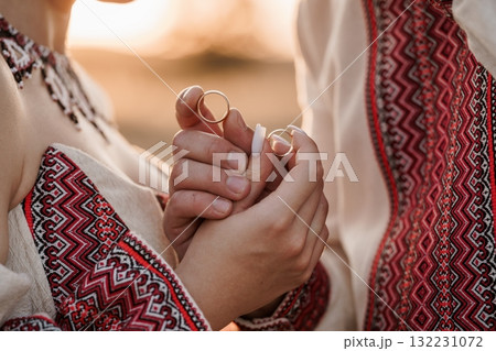 Romantic Wedding Rings Exchange in Traditional Embroidered Clothing, Golden Bands, Close-Up, Warm Sunset Light, Love, Commitment, Ukrainian Style. 132231072