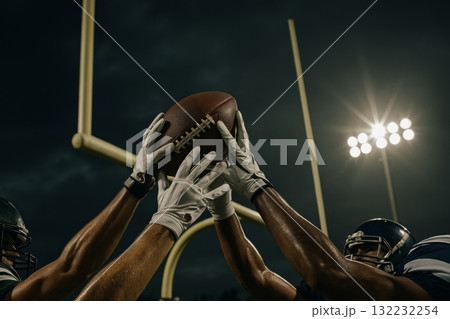 American football players reaching for ball under stadium lights 132232254