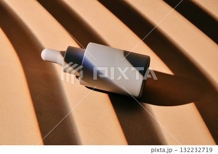 A bottle of serum on a beige background with stripes of shadows. A bottle of serum on a beige background with stripes of shadows. 132232719