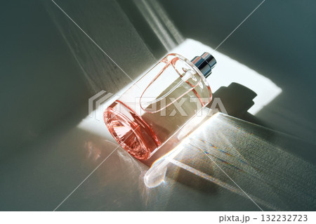 Pink perfume bottle on the light background in the rays of sun with highlights. 132232723