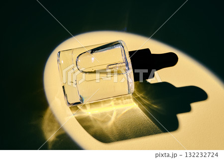 A bottle of face or hair oil in the spotlight on a yellow background. A bottle of face or hair oil in the spotlight on a yellow background. 132232724