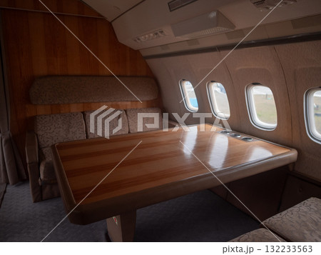 wooden conference table inside airplane cabin with glossy finish and seats, spacious layout suited for corporate meeting, document review and collaborative work during private flight service 132233563