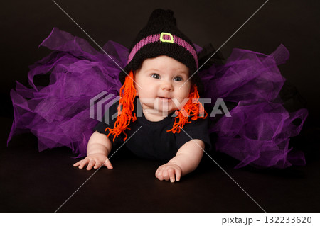 Cute baby in Halloween costume with witch hat and purple tulle skirt on black background 132233620