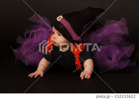 Baby in witch costume with orange yarn hair and purple tulle skirt, looking to the side 132233622