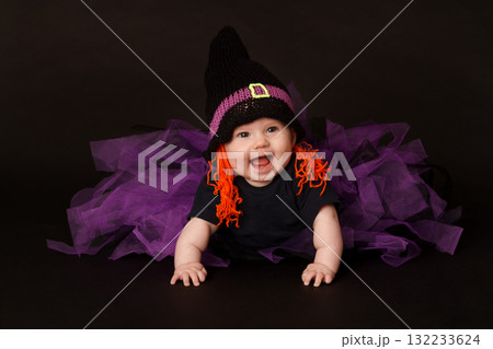 Smiling baby in Halloween witch costume with purple tulle skirt and orange yarn hair 132233624