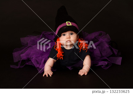 Cute baby in Halloween costume with witch hat and purple tulle skirt on black background 132233625