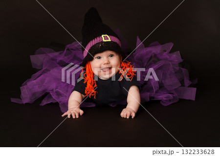 Smiling baby in Halloween witch costume with purple tulle skirt and orange yarn hair 132233628