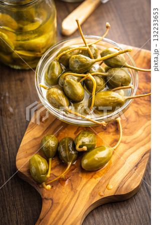 Pickled capers berries in bowl on wooden cutting board. 132233653