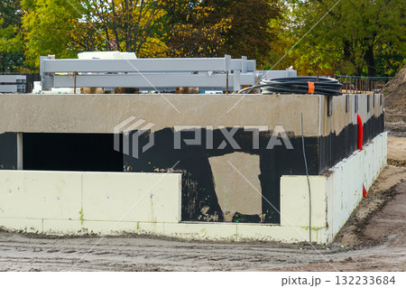 Insulated building foundation with waterproofing and utility pipes at modern construction site 132233684