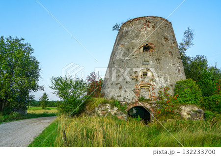 Historic stone windmill tower ruin with brick archway and greenery along rural countryside road 132233700