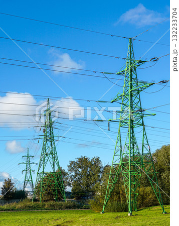 Green electricity pylons with power lines extending across blue sky and rural landscape Green electricity pylons with power lines extending across blue sky and rural landscape 132233704