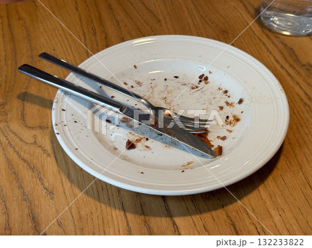 Empty messy dessert plate with crumbs and cutlery on wooden table. Satisfaction, simplicity, and everyday cafe moment after meal. Empty messy dessert plate with crumbs and cutlery on wooden table. Satisfaction, simplicity, and everyday cafe moment after meal. 132233822