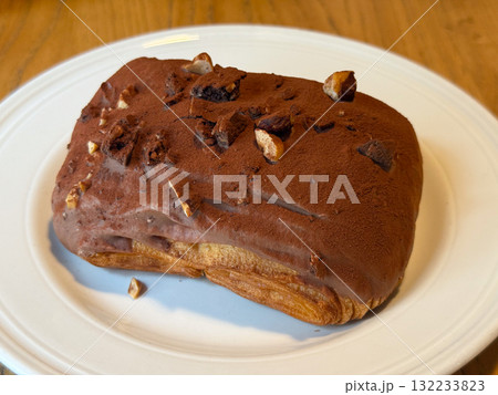 Chocolate-covered pastry with nuts on white plate. Sweetness, texture, and indulgence in artisanal dessert presentation. Chocolate-covered pastry with nuts on white plate. Sweetness, texture, and indulgence in artisanal dessert presentation. 132233823