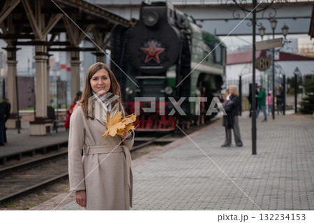 Woman with autumn leaves on her shoulder stands near an old steam locomotive at a railway station in Moscow Woman with autumn leaves on her shoulder stands near an old steam locomotive at a railway station in Moscow 132234153