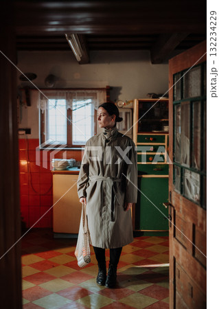 Woman standing in old rural kitchen with half-empty shopping bag. Woman standing in old rural kitchen with half-empty shopping bag. 132234229