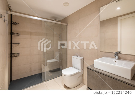 Modern bathroom with a glass shower, white toilet, and sleek sink. Neutral tile walls and floor create a clean, minimalist aesthetic. 132234240