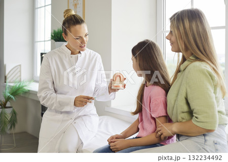 Dentist teaching child and mother tooth brushing with model during pediatric visit 132234492