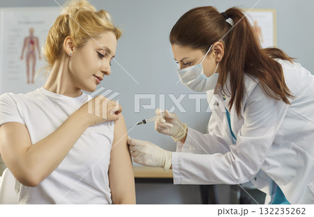 Masked doctor administering vaccine injection to adult patient in bright clinic Masked doctor administering vaccine injection to adult patient in bright clinic 132235262