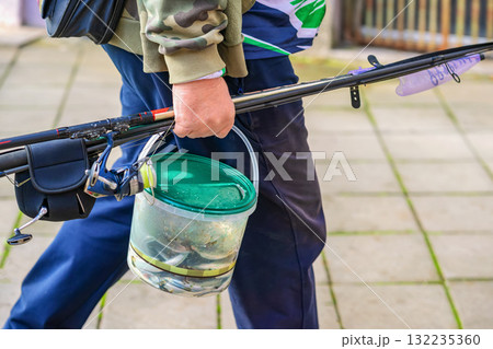 Close-up of fisherman holding fishing rods and bucket full of fresh catch walking on paved city street. Concept of fishing, outdoor hobby, fresh seafood Close-up of fisherman holding fishing rods and bucket full of fresh catch walking on paved city street. Concept of fishing, outdoor hobby, fresh seafood 132235360