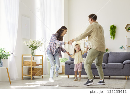 Happy parents dancing with daughter at home living room, joyful family bonding Happy parents dancing with daughter at home living room, joyful family bonding 132235411