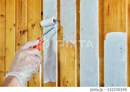 House painter applies white paint with roller on wooden panels. House painter applies white paint with roller on wooden panels. 132236349