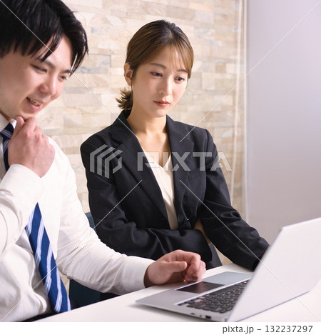 オフィスでパソコンを見ながら打ち合わせをする若い男女 132237297