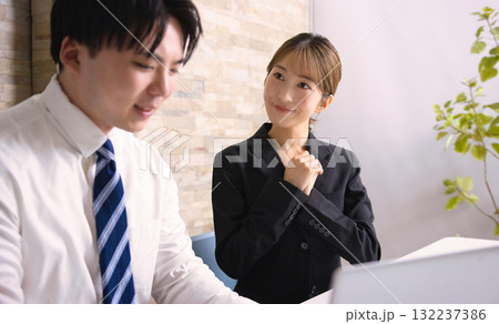 オフィスでパソコンを見ながら打ち合わせをする若い男女 オフィスでパソコンを見ながら打ち合わせをする若い男女 132237386