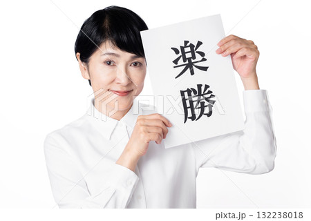 楽勝と書かれた紙を持ち目線を送る白いシャツを着たシニア女性 132238018