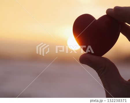 Hand holding a red heart with the sun in the background Hand holding a red heart with the sun in the background 132238371
