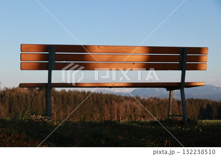 The bench is empty and the sun is shining on it, creating a peaceful 132238510