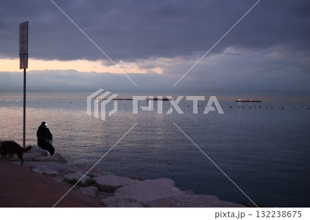 Man sits on a rock by the water, watching the boats in the distance 132238675