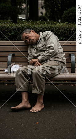 公園の隅っこでベンチで寝るホームレス 132241067