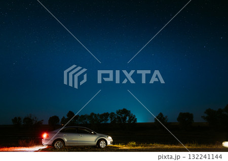 Car Sedan Parking On A Roadside Of Country Road On A Background Of Blue Sky At Winter Season. Country Asphalt Road In Countryside. Night View Of Natural Glowing Stars. Ground In Lights From Rear Red Car Sedan Parking On A Roadside Of Country Road On A Background Of Blue Sky At Winter Season. Country Asphalt Road In Countryside. Night View Of Natural Glowing Stars. Ground In Lights From Rear Red 132241144
