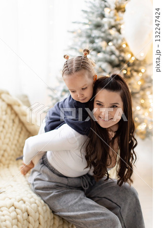 A mother and daughter share a loving moment during the Christmas season, with a decorated tree in the background. 132247424