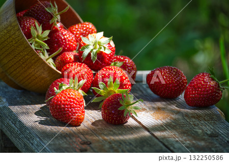 Fresh strawberries spilling from wooden bowl on rustic table 132250586
