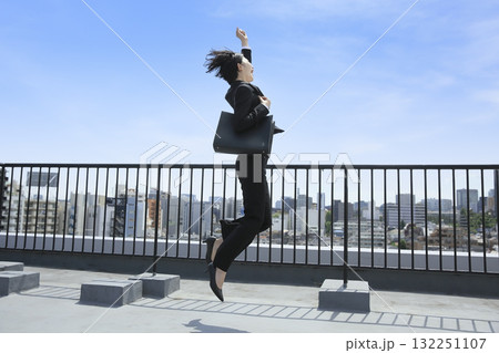 青空の下でジャンプするスーツ姿のビジネスウーマン 132251107