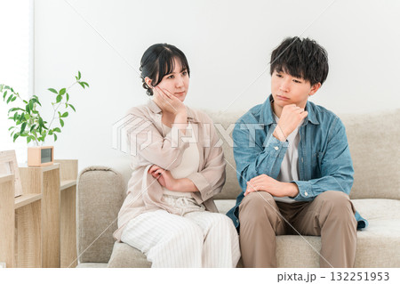 リビングのソファーに座りながら悩み事を相談する夫婦,カップルの若いアジア人 リビングのソファーに座りながら悩み事を相談する夫婦,カップルの若いアジア人 132251953
