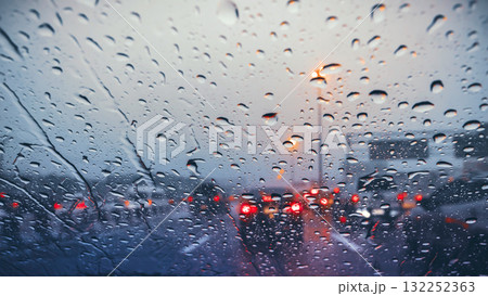 Atmospheric view of heavy rain on the highway at dusk, with raindrops on the windshield and blurred taillights 132252363