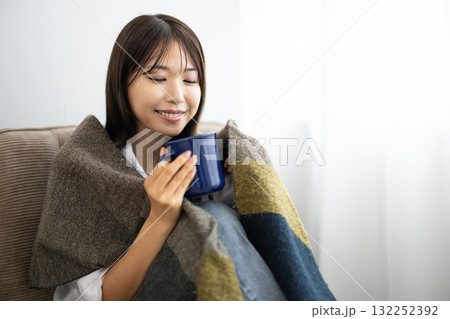 窓辺でブランケットをかけて暖かい飲み物を楽しむ若い女性 窓辺でブランケットをかけて暖かい飲み物を楽しむ若い女性 132252392