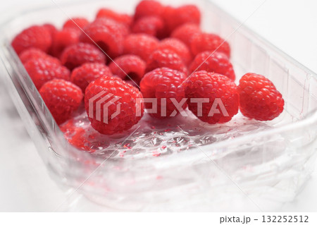 Fresh raspberries in plastic transparent supermarket packaging on a white table surface Fresh raspberries in plastic transparent supermarket packaging on a white table surface 132252512