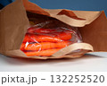 Carrots wrapped in clear plastic inside a paper bag on a table 132252520