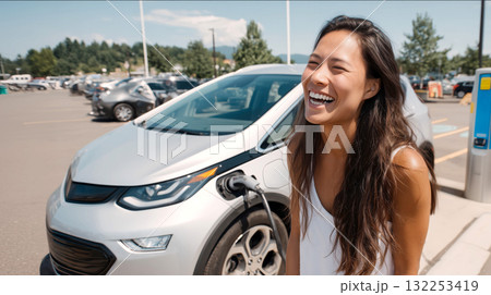 Young Asian woman laughing while charging electric SUV in grocery store parking lot, bright sunny day, natural lighting, candid lifestyle 132253419