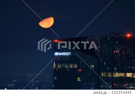 Early half harvest moon in Tokyo over the new Takanawa Gateway Marriott Hotel in the early evening in Minato-ku Tokyo Japan 132253445