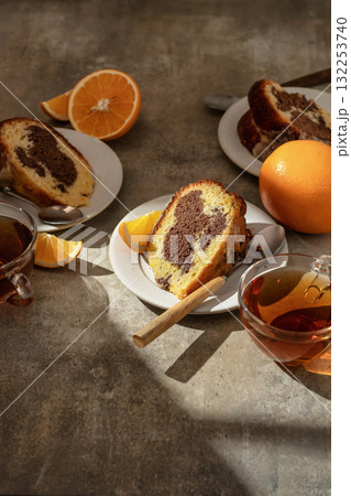 Piece of orange and chocolate marble bundt cake in bright morning light with clear shadows. Fruity citrus dessert on green textured background 132253740