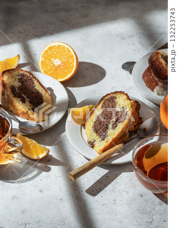Piece of orange and chocolate marble bundt cake in bright morning light with clear window shadows. Fruity citrus dessert on light gray kitchen background 132253743