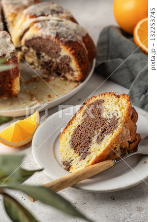 Piece of orange and chocolate marble bundt cake with sugar icing close up. Fruity citrus dessert on light gray kitchen background Piece of orange and chocolate marble bundt cake with sugar icing close up. Fruity citrus dessert on light gray kitchen background 132253745
