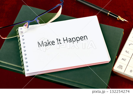 A note saying Make It Happen rests on a spiral notebook in a workspace. Glasses and a pen accompany it, reflecting a moment of focus and ambition in achieving goals A note saying Make It Happen rests on a spiral notebook in a workspace. Glasses and a pen accompany it, reflecting a moment of focus and ambition in achieving goals 132254274