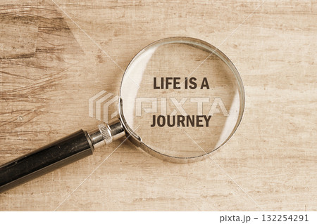 A magnifying glass rests on a wooden table, focusing on the phrase life is a journey. This setup invites contemplation about personal growth and adventure 132254291