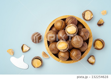 Macadamia nuts in wood bowl with broken macadamia on blue background, top view Macadamia nuts in wood bowl with broken macadamia on blue background, top view 132254628
